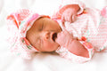 Newborn baby wrapped in a pink and white patterned blanket with a matching hat on a white background